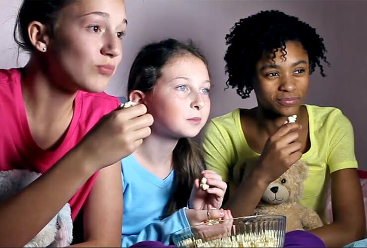 Diverse group of young girls with popcorn stare transfixed at the TV