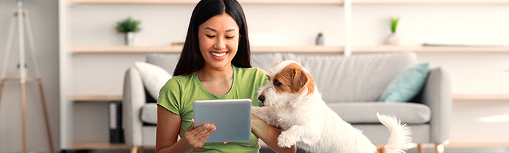 Woman with small fluffy dog quickly browses her tablet before walk time