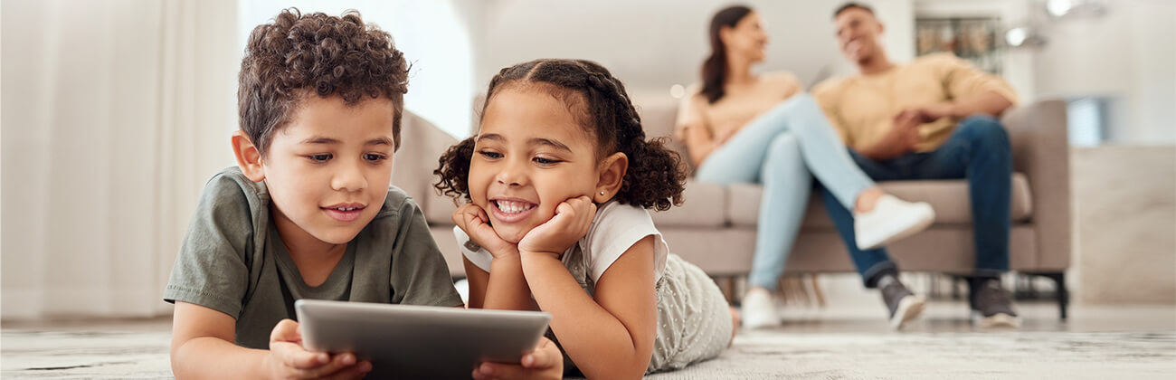 Two kids use a tablet with mom and dad in the background