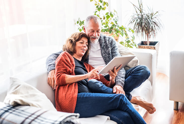 Retired couple reviews cybersecurity resources on a tablet from the comfort of their sofa